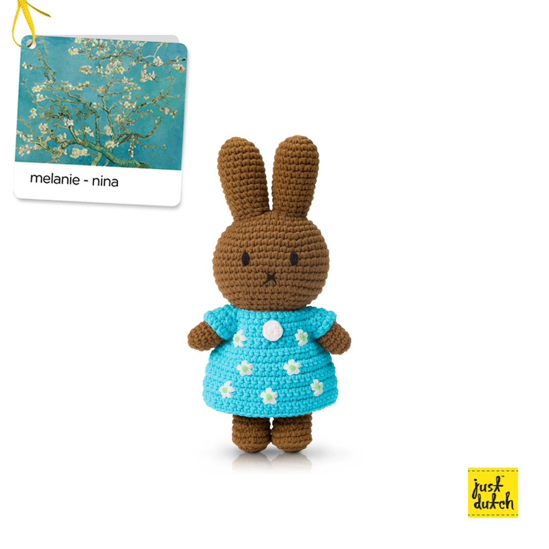 Crocheted rabbit toy in a blue dress with white flowers, standing next to a book titled 'melanie - nina'.